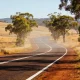 An empty two-lane country highway curving through dry golden paddocks and gum trees on a bright afternoon in the NSW Southern Highlands